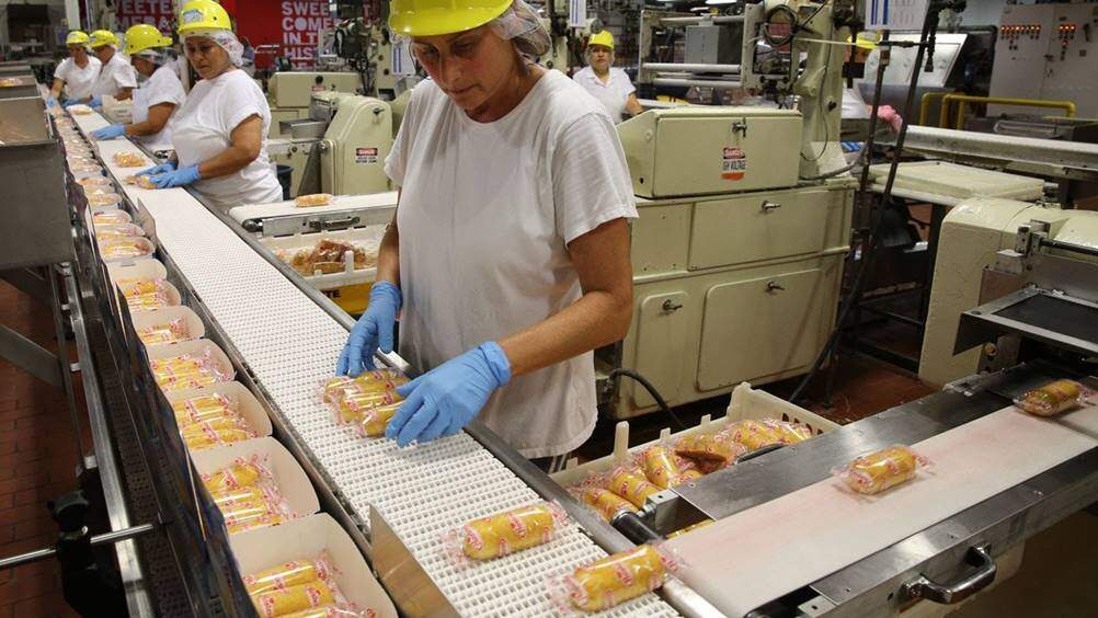 Mulher trabalhando em uma linha de produção, a qual se baseia em um Layout de produção